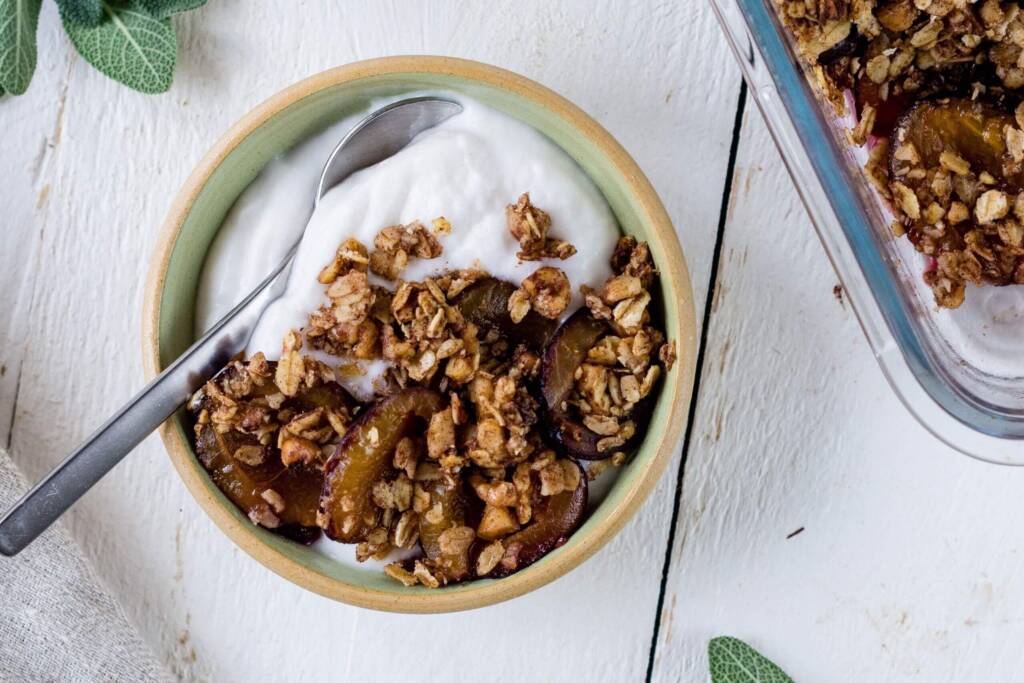 Pflaumen-Crumble mit Zimt in einer Schüssel auf weissem Holztisch